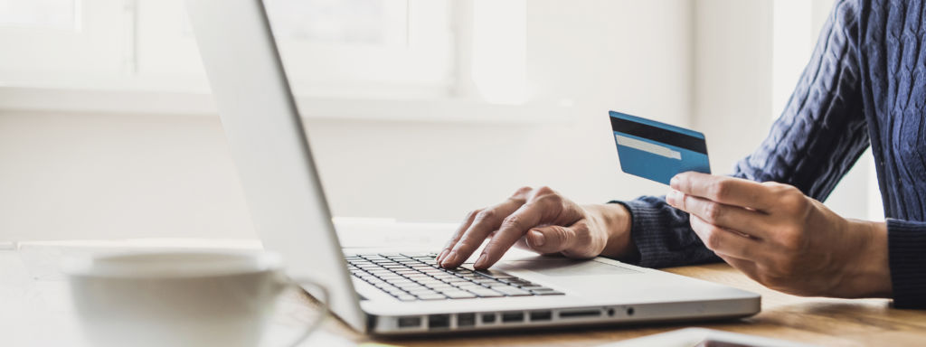 Homem realizando compras online por meio de um laptop, utilizando um cartão de crédito.